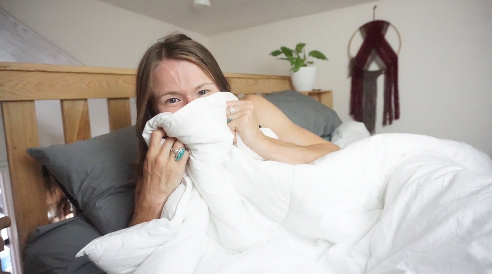 Sustainable Jungle's Head of Content, Amber, smiling and wrapped in a fluffy white organic comforter on a wooden bed, representing the best non-toxic and sustainable bedding options by Sustainable Jungle.
