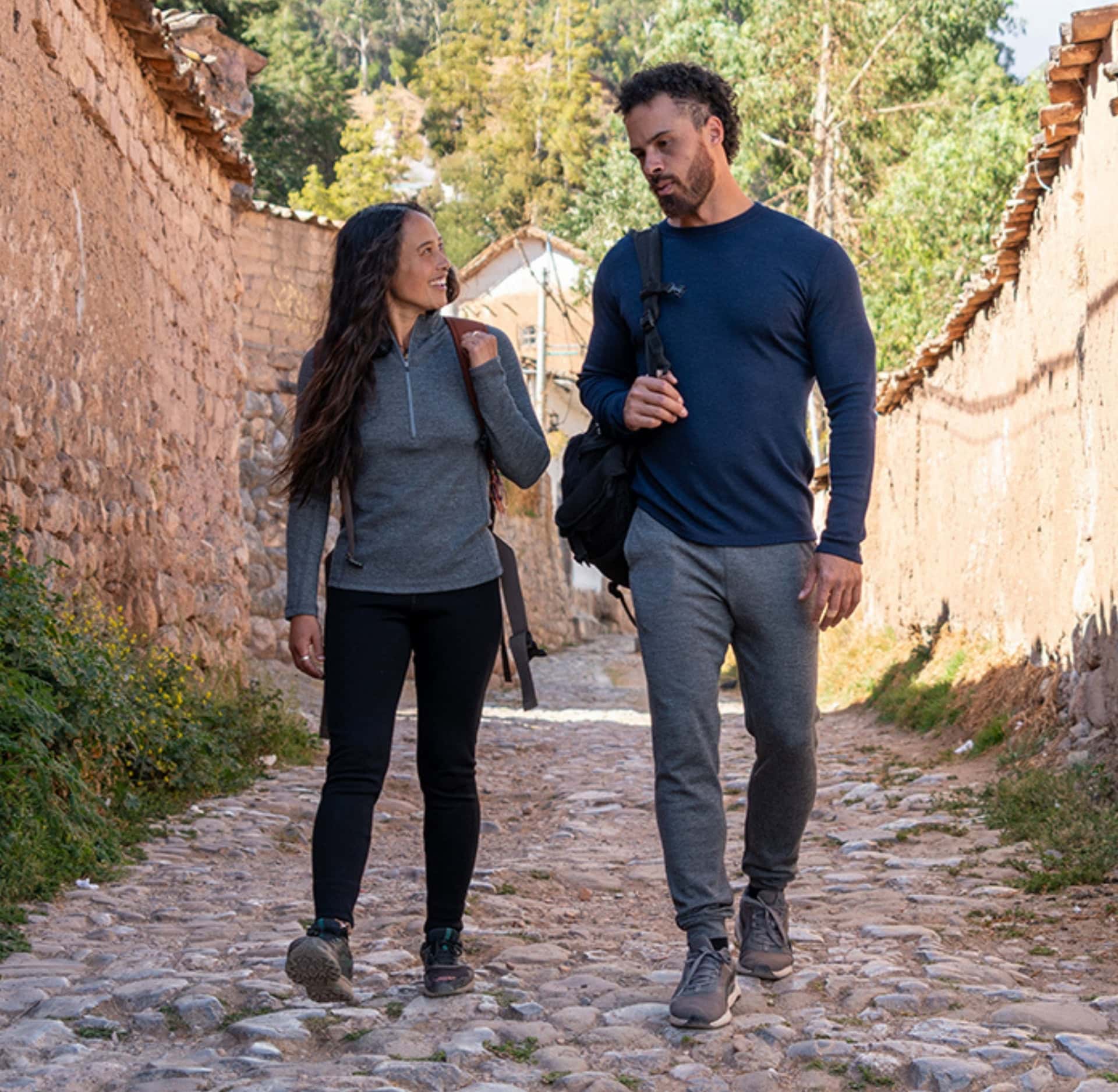 A woman and man are walking along cobblestones together. She is wearing a grey alpaca half-zip top by Arms of Andes. He wears an Arms of Andes top and pants. This image is featured in the Sustainable Jungle Brand Directory listing for Arms of Andes.